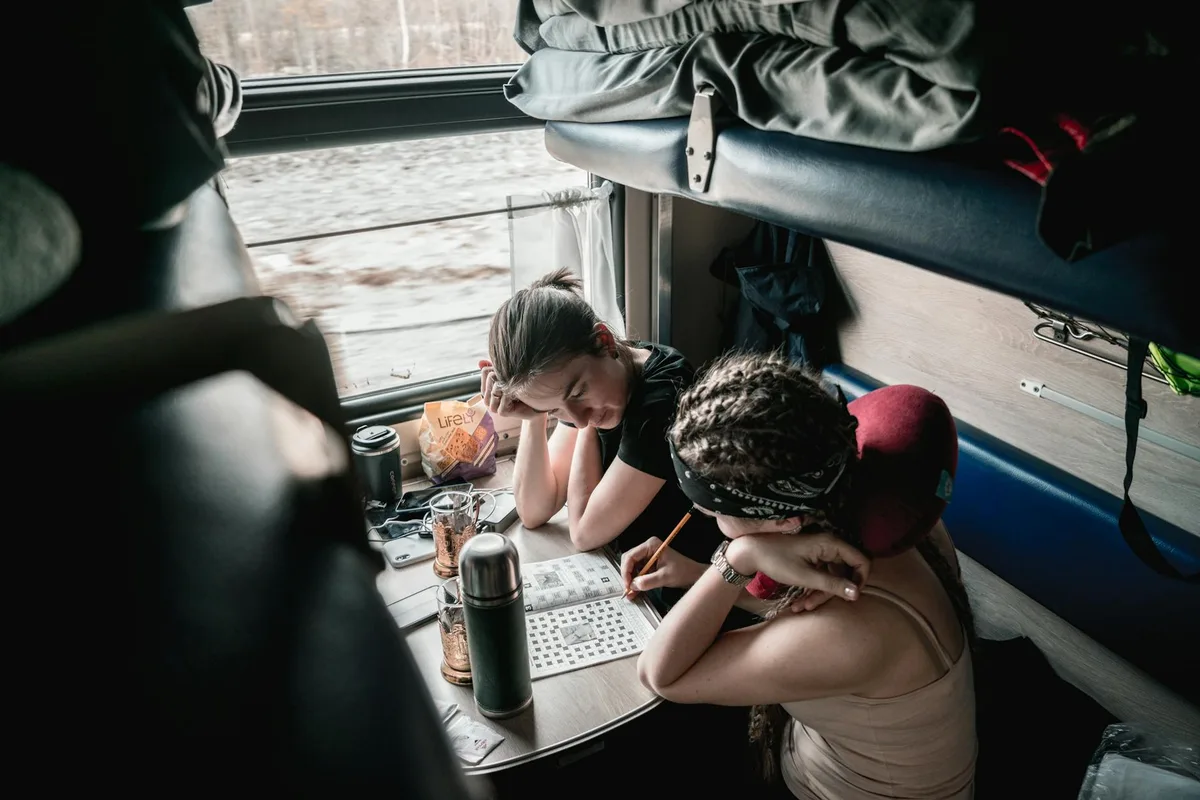Two women enjoy solving puzzles during a relaxing train ride, capturing a moment of thoughtful leisure.
