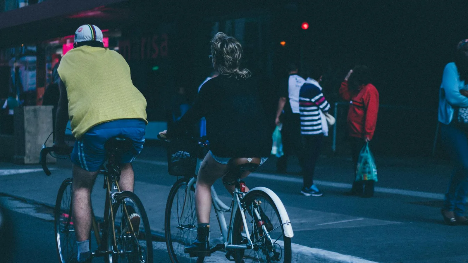 Two cyclists biking on a busy urban street with pedestrians nearby.