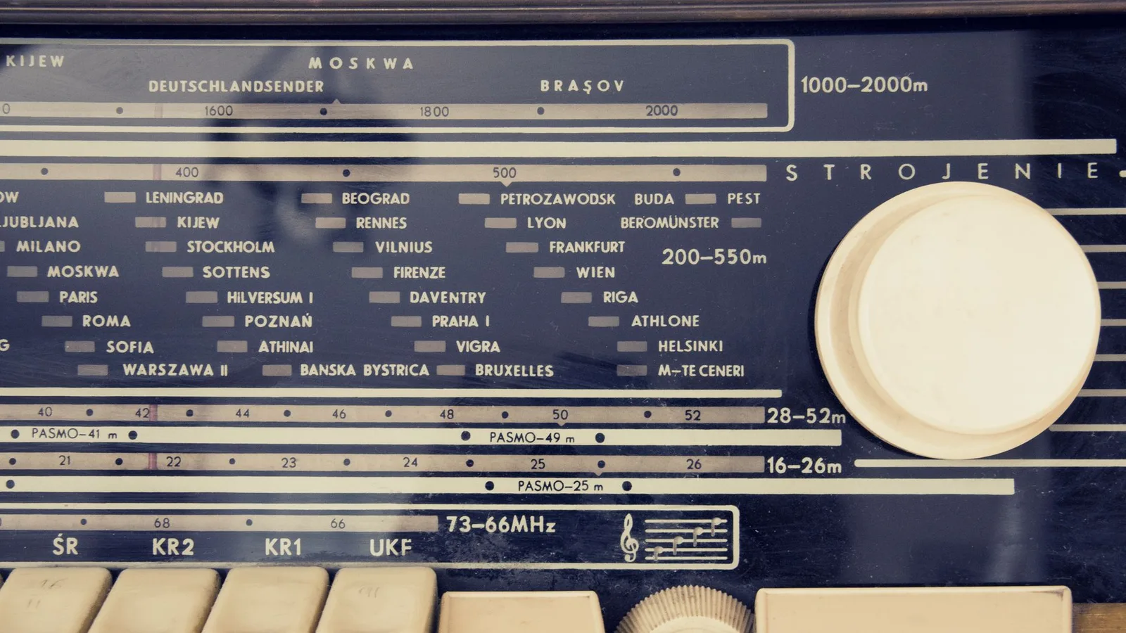 A detailed view of a vintage radio's tuning dial with city stations displayed.