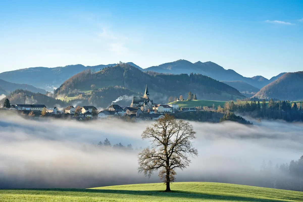 A picturesque view of Maria Neustift village surrounded by fog and mountains in the morning sun.