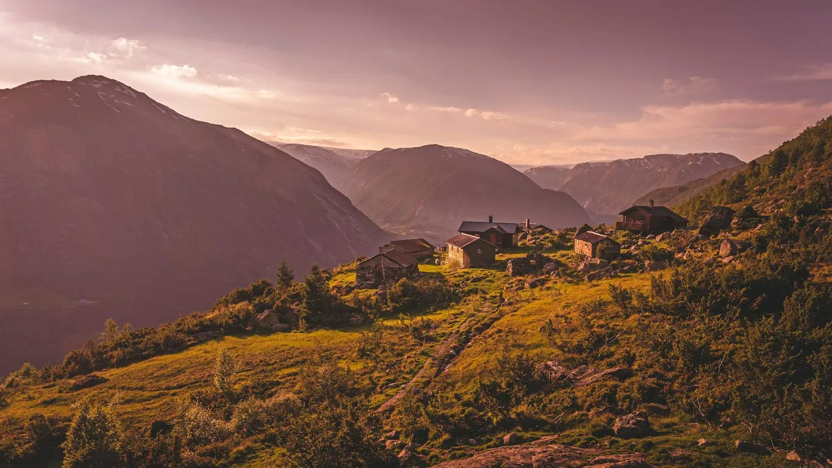 A serene mountain village with wooden cabins nestled on a lush hilltop during dusk.