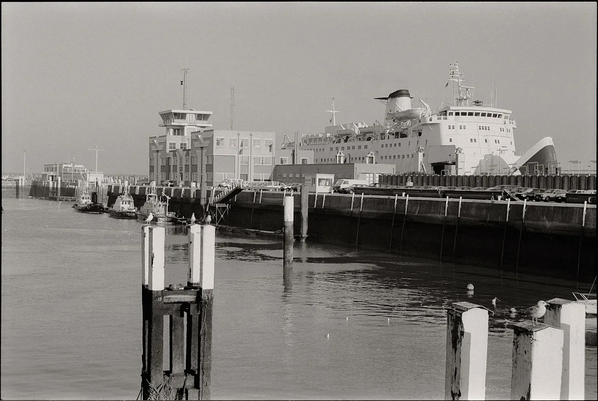 Black and white photo of a harbor with a large ship docked by a terminal.