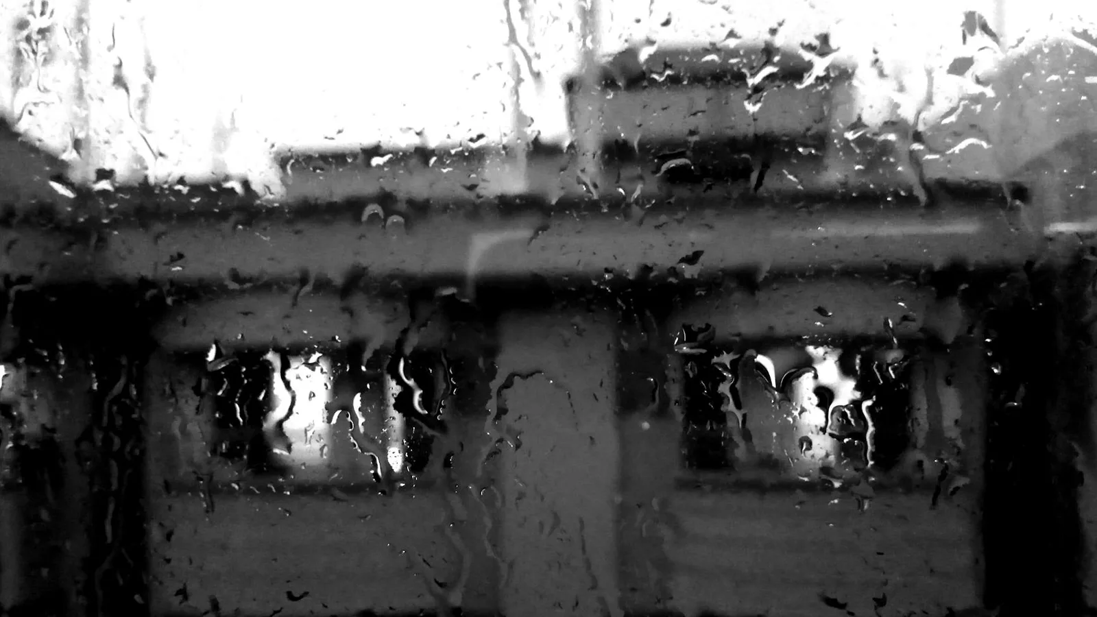 Black and white image of a building seen through rain-covered window in Dhaka.