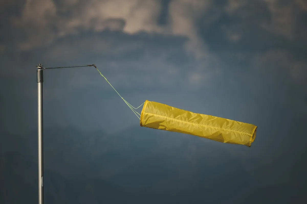 An isolated yellow windsock indicating wind direction against a dark, cloudy backdrop.