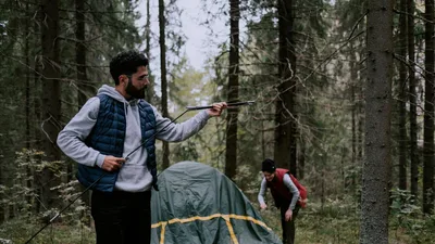 A couple assembling a tent in a wooded forest, enjoying an outdoor camping adventure.