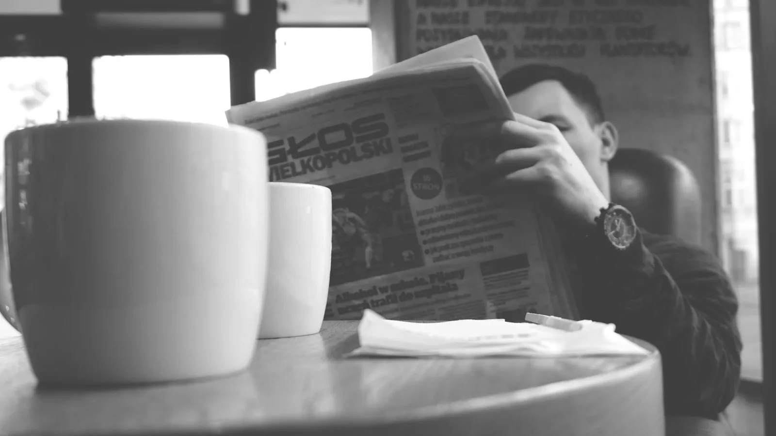 Adult man enjoying a relaxing moment in a café, reading a newspaper with a cup of coffee nearby.