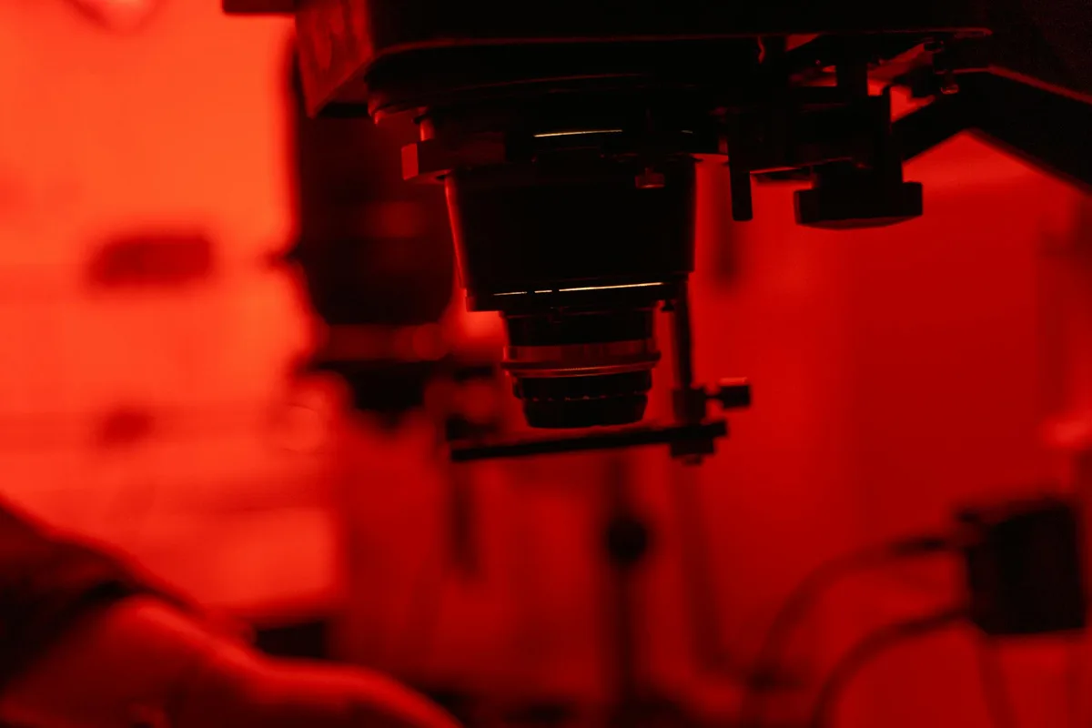 Enlarger equipment in a red-lit darkroom, used for developing photographs.