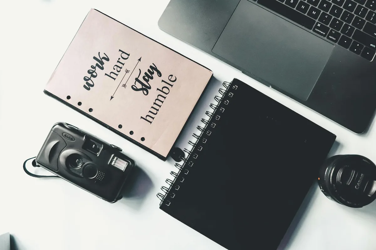 Flat lay composition of black netbook with analog photo camera and notebooks placed on white surface of desk