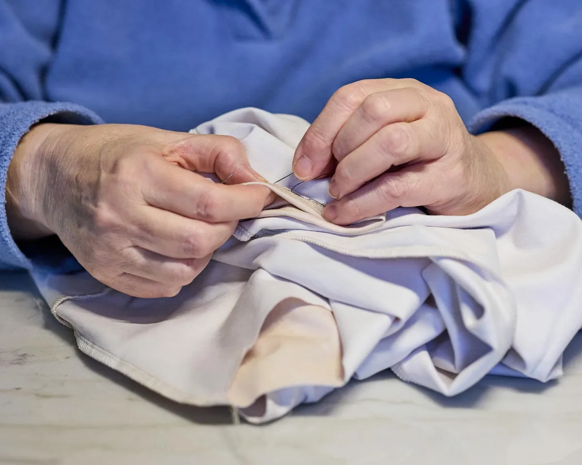 Detailed image of hands sewing white fabric, showcasing precision and skill in a traditional craft.
